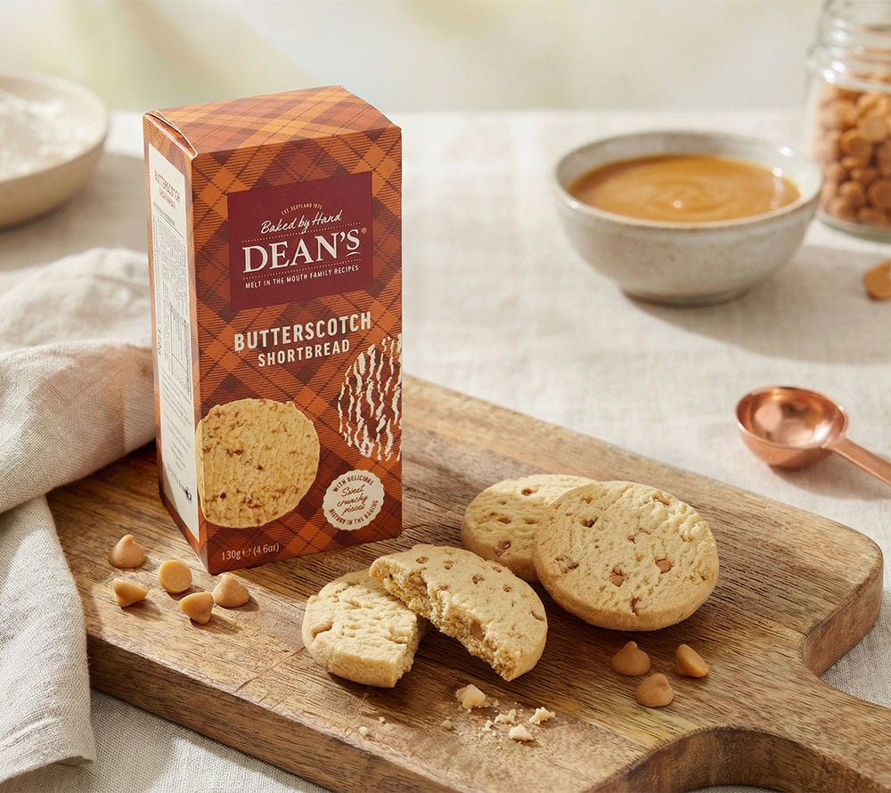 Dean's Butterscotch Shortbread Pappschachtel mit Keksen und Butterscotch‑Chips auf Schneidebrett neben Karamellsauce – gourmet Produktbild.
